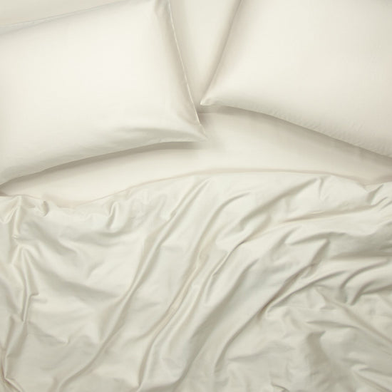Birds eye view of organic cotton fitted bedding set with pillowcases, fitted sheet and quilt cover in egg shell white