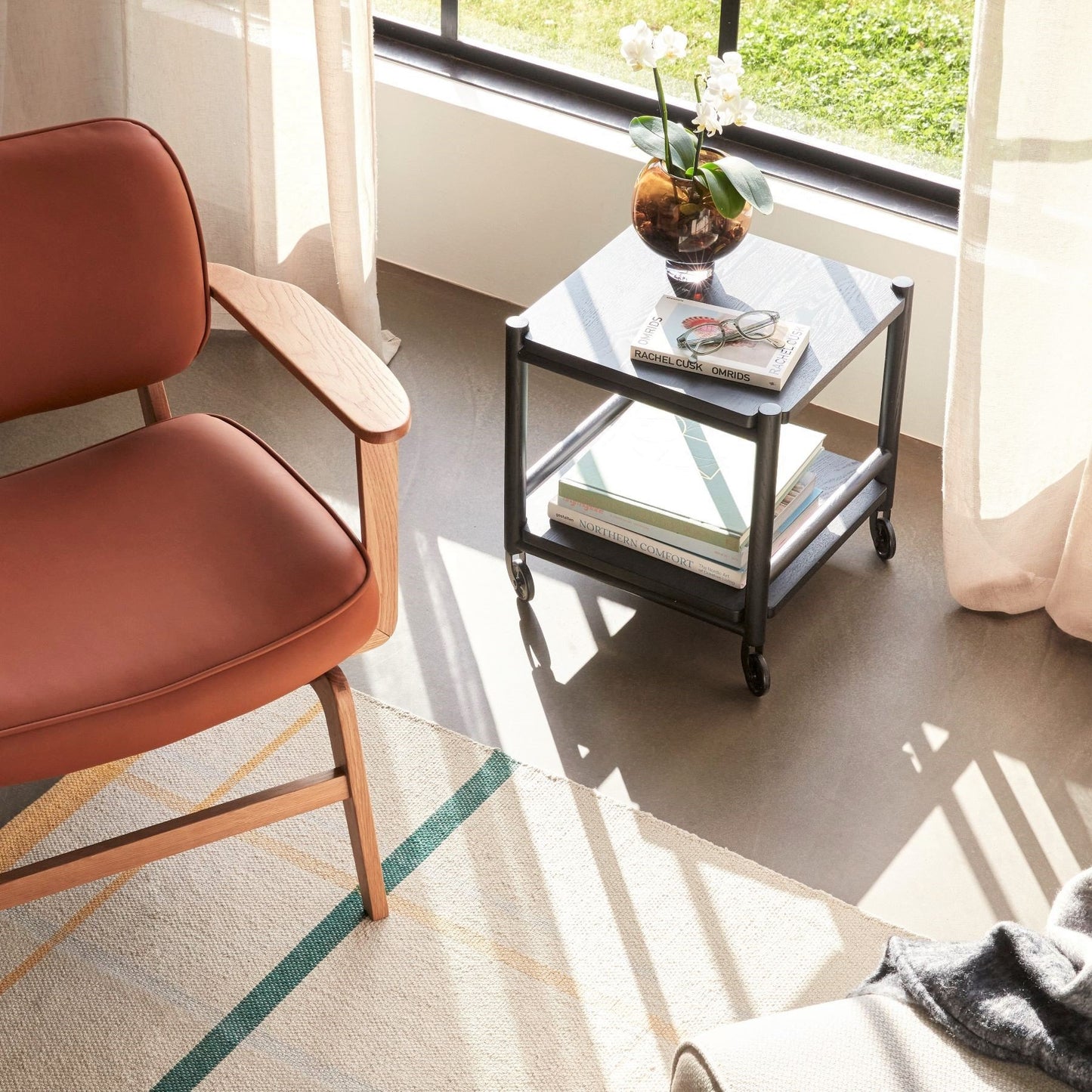 Hubsch Interior Nordic designer cocoon vase in brown glass with an orchid plant sitting inside on a side table with a book