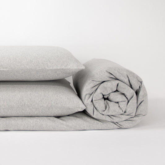 Stack of organic jersey quilt cover set with pillowcases and rolled up quilt cover in cloud grey