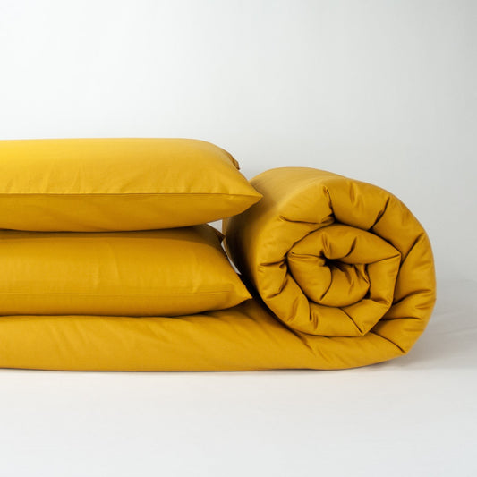 Stack of organic cotton quilt cover set with pillowcases and rolled up quilt cover in honey gold