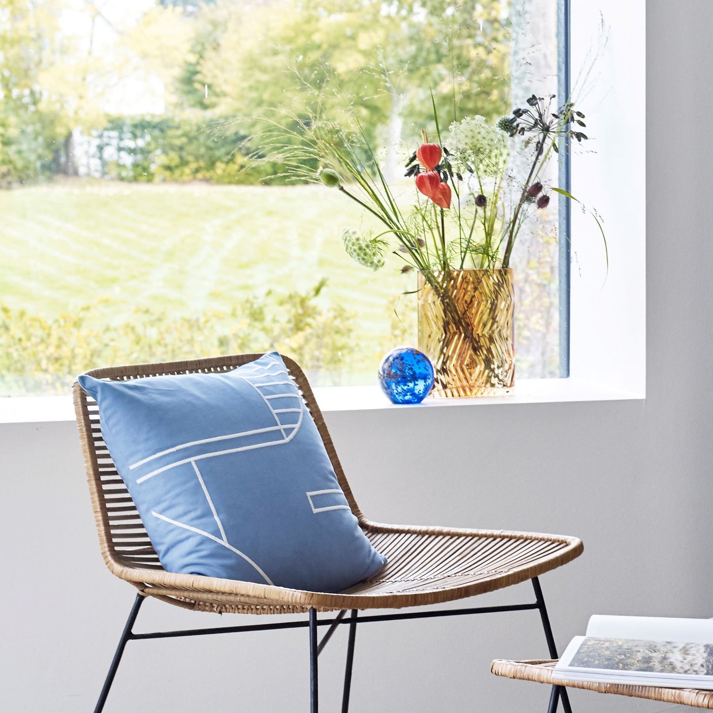 Hubsch Interior Nordic designer diamond textured vase in amber glass inside on a window sill with flowers and a rattan chair