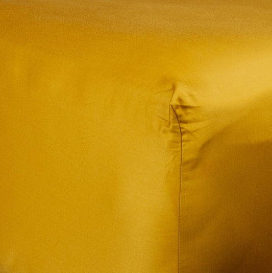 Corner of bed with organic cotton fitted sheet in honey gold