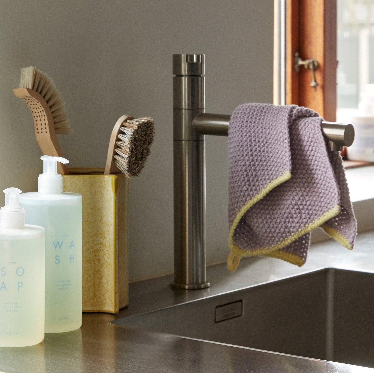 Hubsch Interior Scandi designer tea towel in lilac purple and yellow cotton knit lying on a kitchen bench hanging on tap