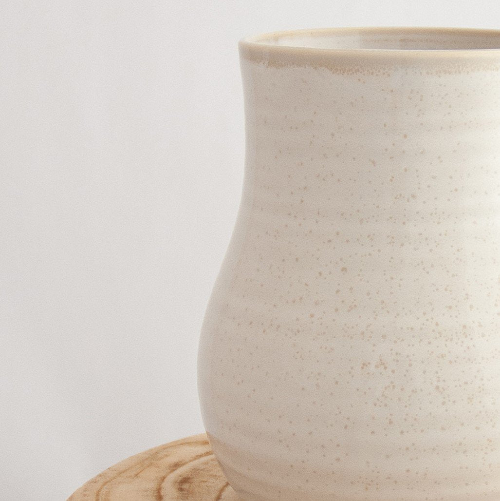 Close up of a Robert Gordon pottery botanica coast white vase sitting on a natural wooden round side table
