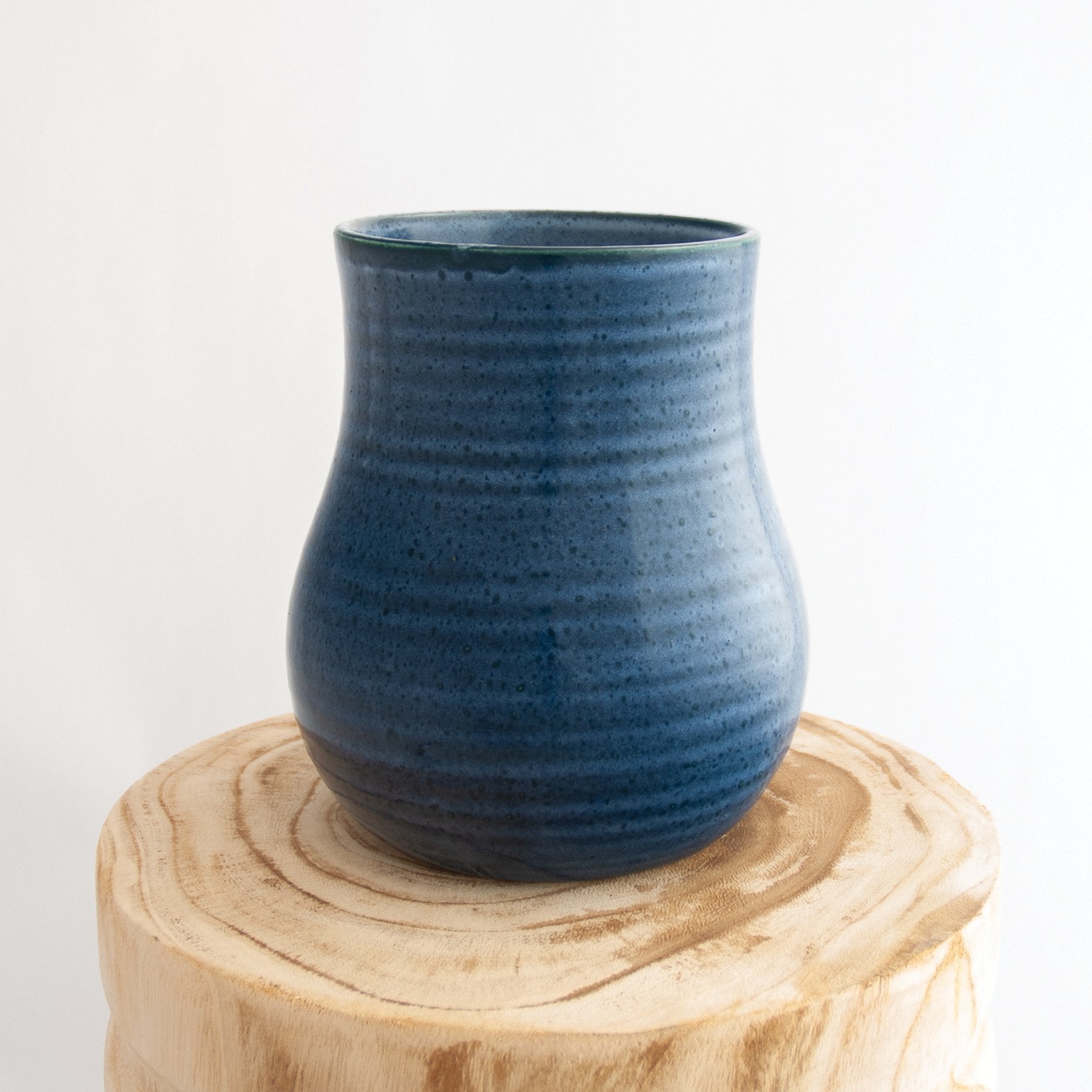 Robert Gordon pottery botanica dark topaz blue vase sitting on a natural wooden round side table