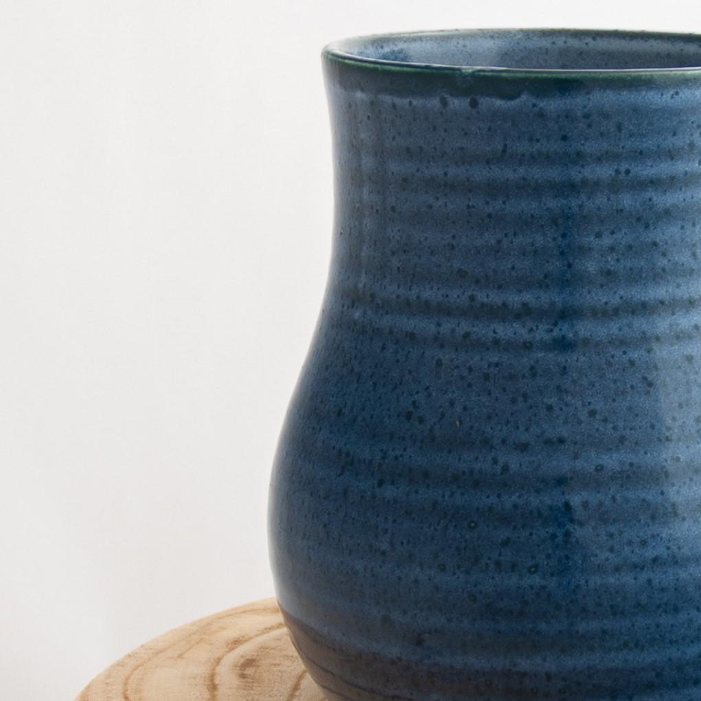 Close up of a Robert Gordon pottery botanica dark topaz blue vase sitting on a natural wooden round side table