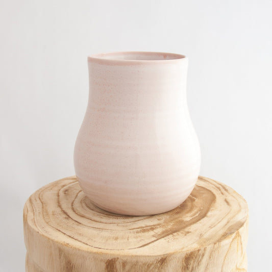Robert Gordon pottery botanica rose quartz pink vase sitting on a natural wooden round side table