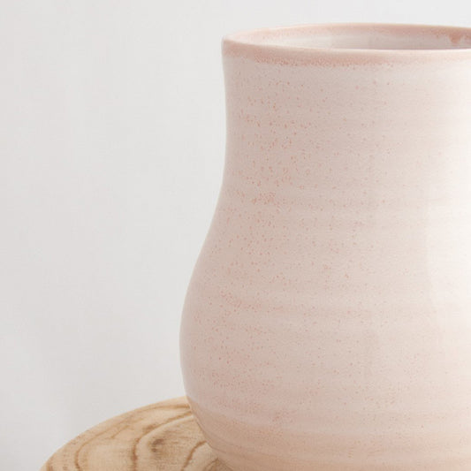 Close up of a Robert Gordon pottery botanica rose quartz pink vase sitting on a natural wooden round side table