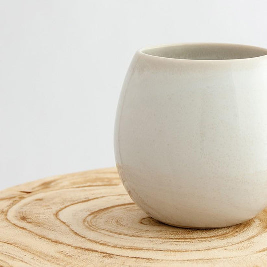 Close up of a Robert Gordon coast white canvas mug coffee cup sitting on a natural wooden round side table