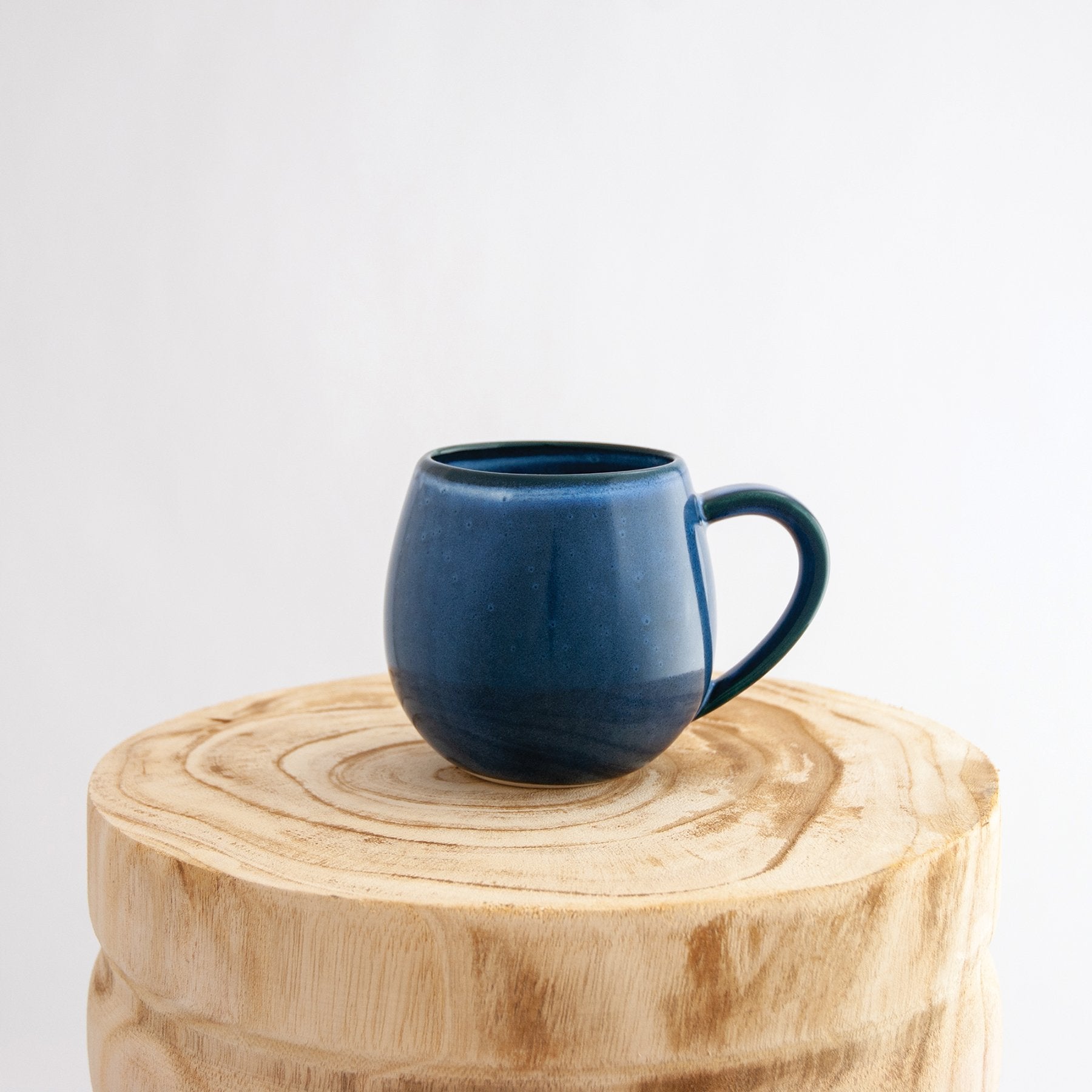 Robert Gordon dark topaz blue canvas mug coffee cup sitting on a natural wooden round side table