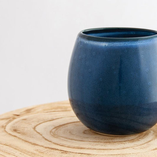 Close up of a Robert Gordon dark topaz blue canvas mug coffee cup sitting on a natural wooden round side table