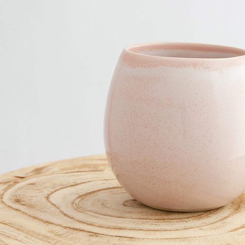Close up of a Robert Gordon rose quartz pink canvas mug coffee cup sitting on a natural wooden round side table