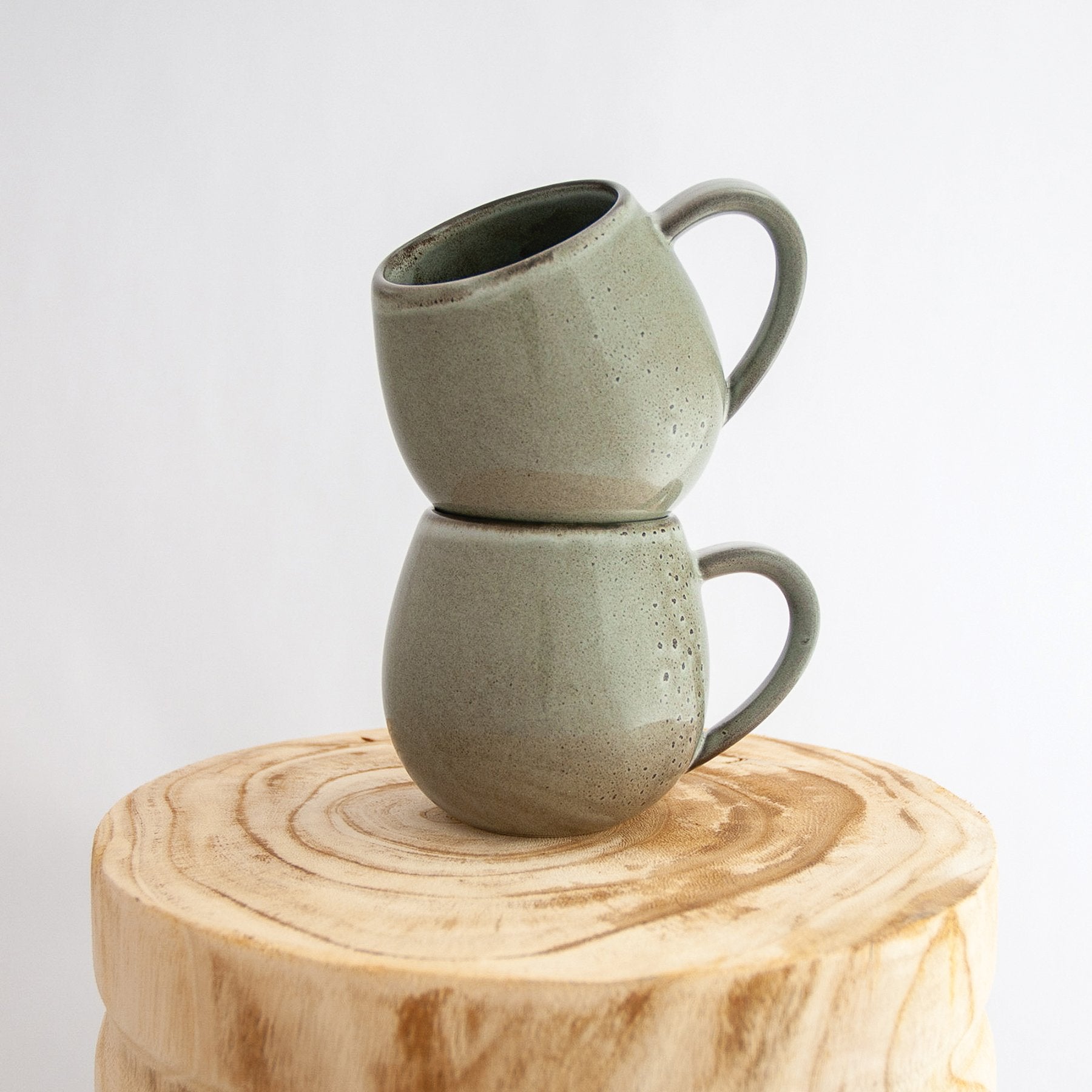 Two Robert Gordon banksia grey canvas mugs stacked on a natural wooden round side table
