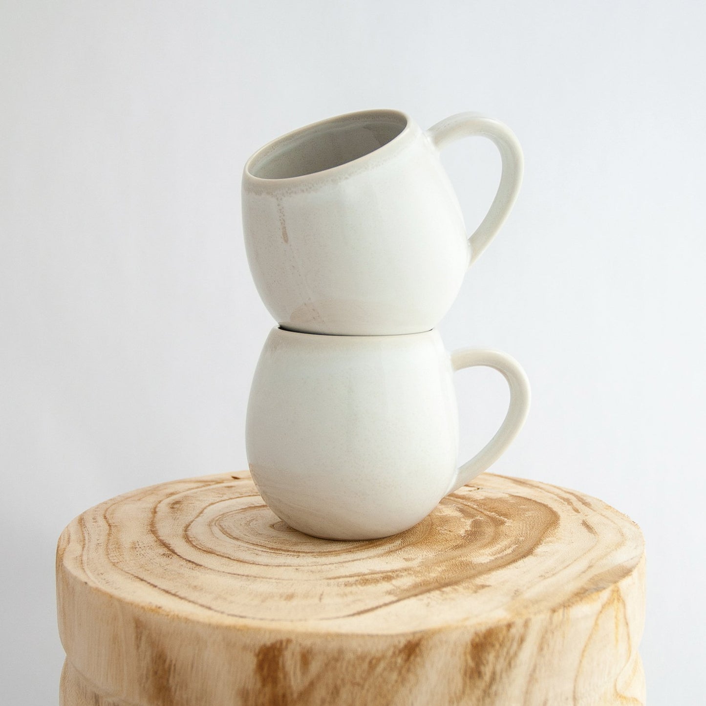 Two Robert Gordon coast white canvas mugs stacked on a natural wooden round side table