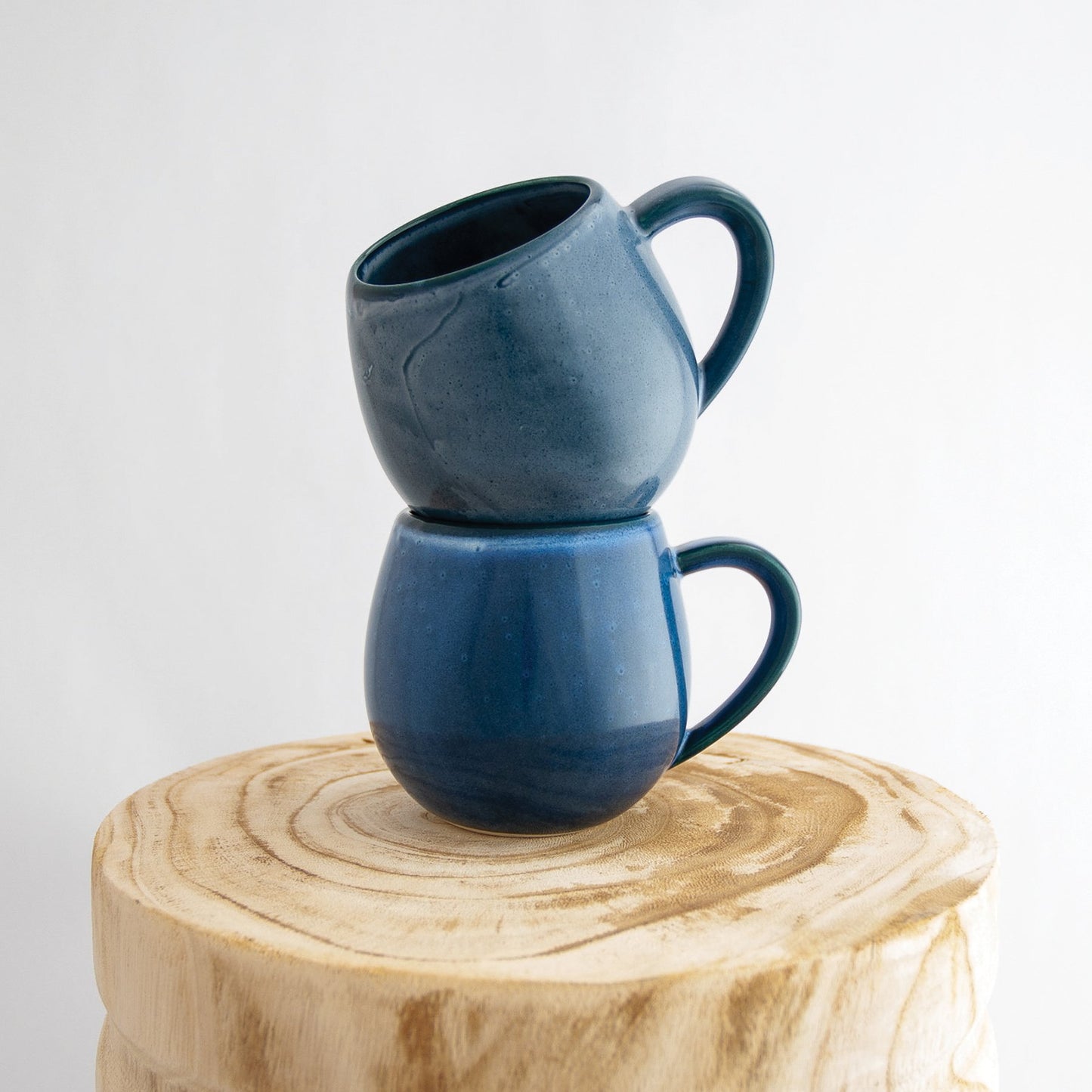 Two Robert Gordon dark topaz blue canvas mugs stacked on a natural wooden round side table
