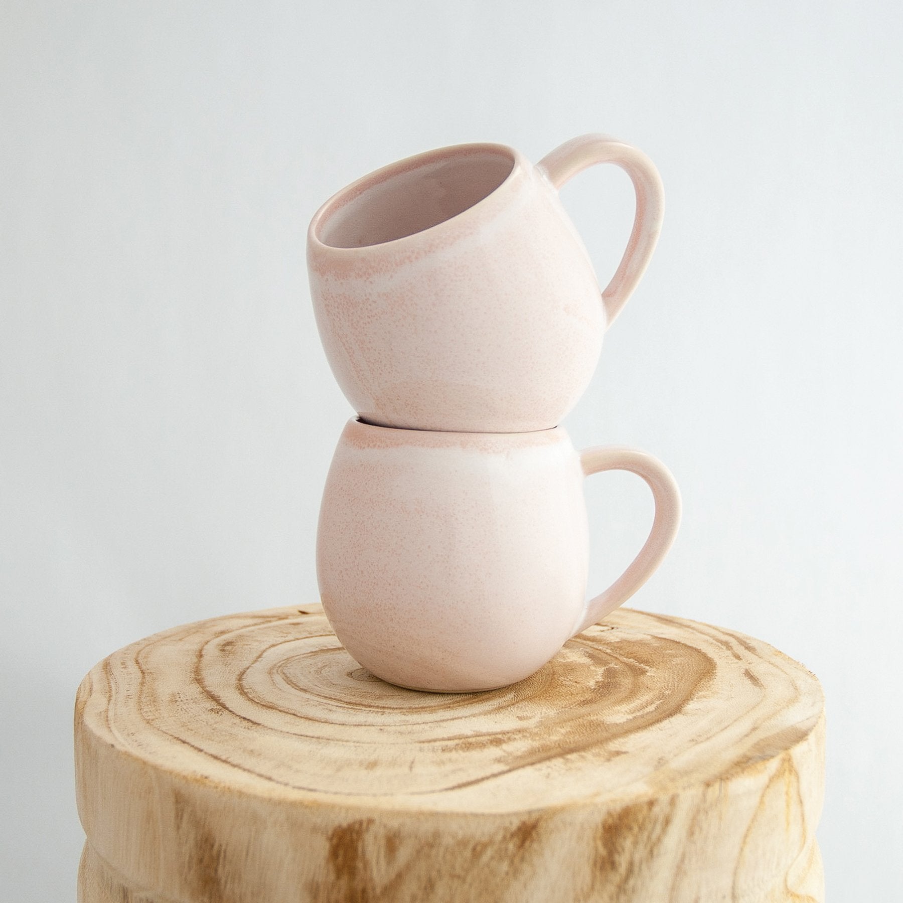 Two Robert Gordon rose quartz pink canvas mugs stacked on a natural wooden round side table