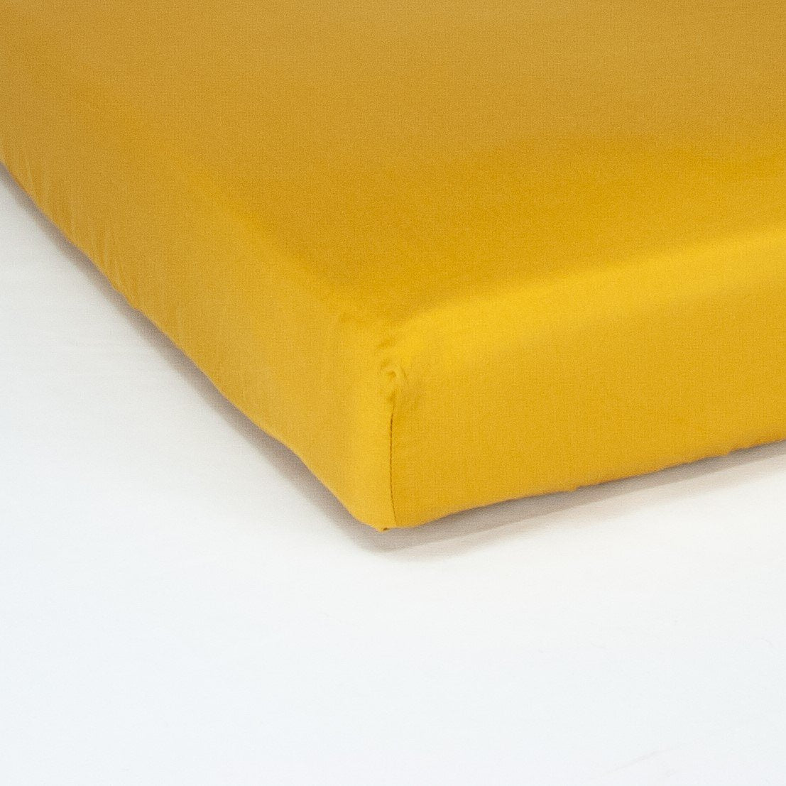 Corner of mattress with organic cotton fitted cot sheet in honey gold