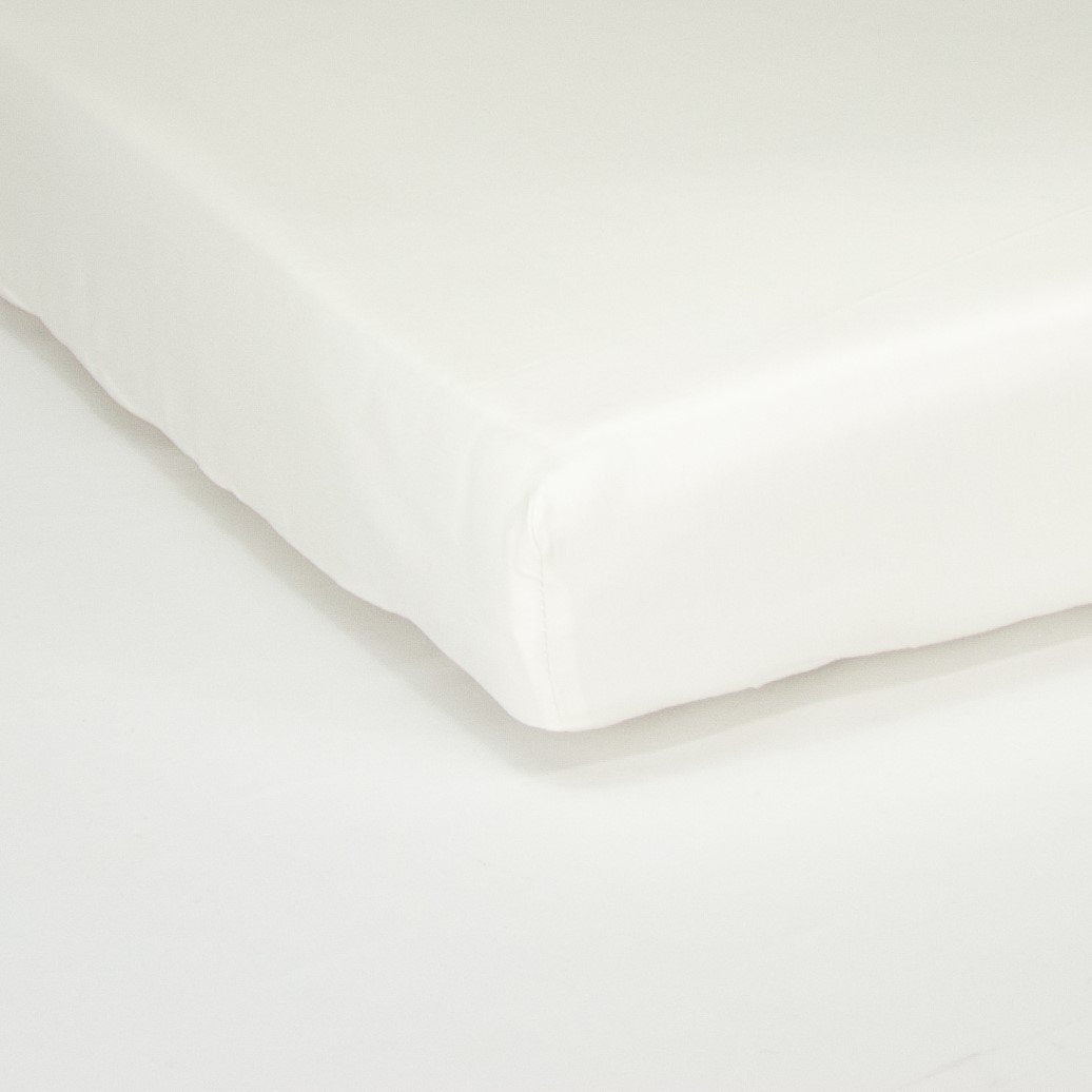 Corner of mattress with organic cotton fitted cot sheet in warm white