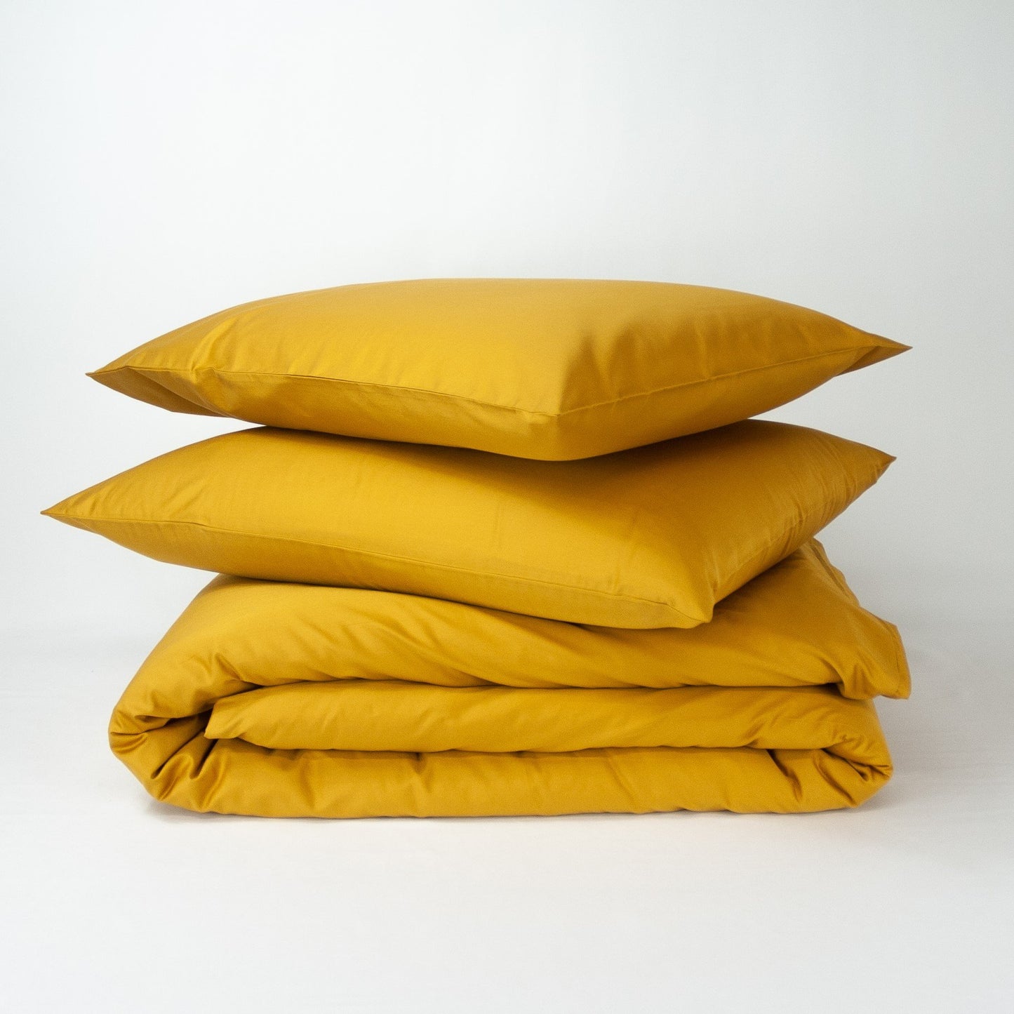 Stack of organic cotton quilt cover set with pillowcases and folded quilt cover in honey gold