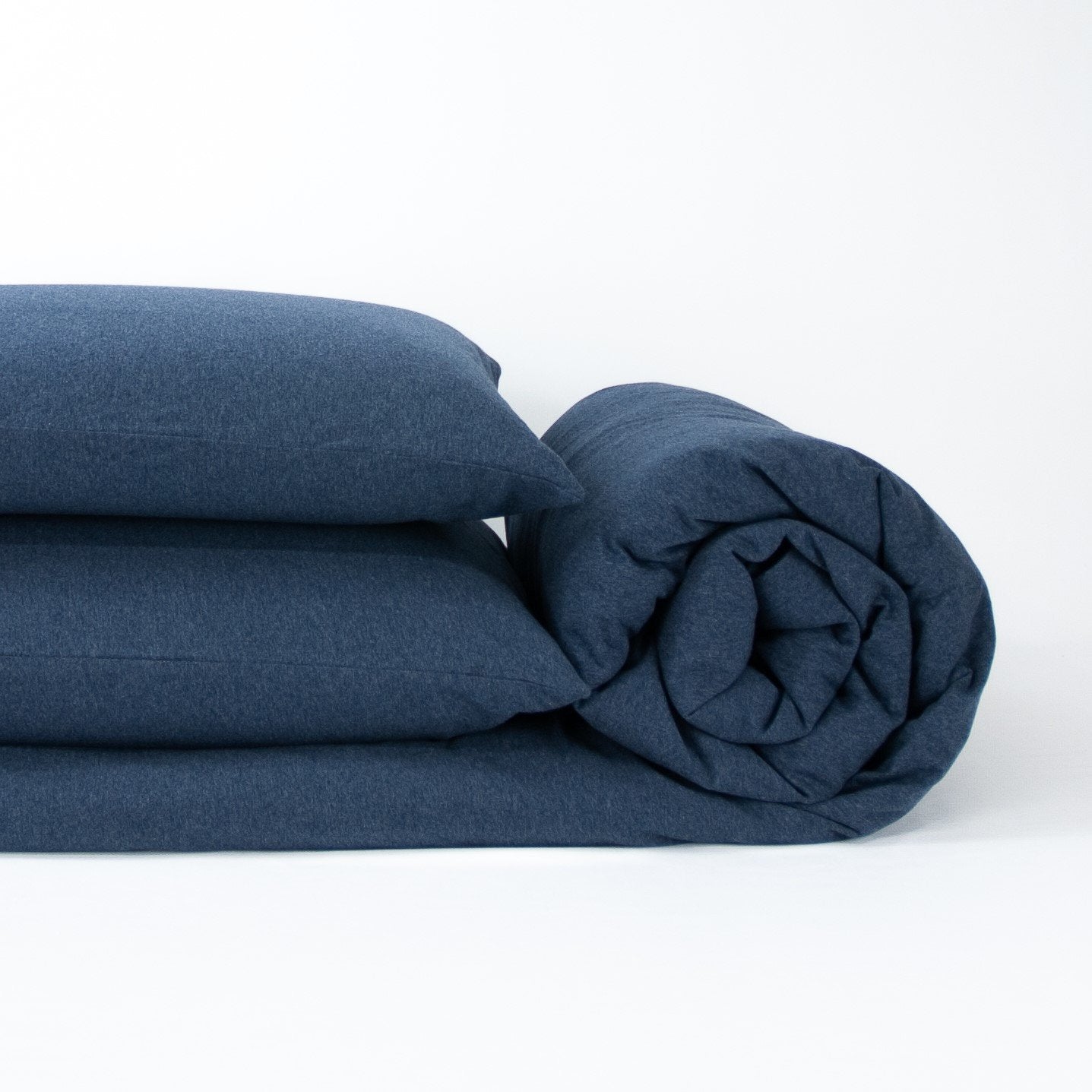 Stack of organic jersey quilt cover set with pillowcases and rolled up quilt cover in indigo blue