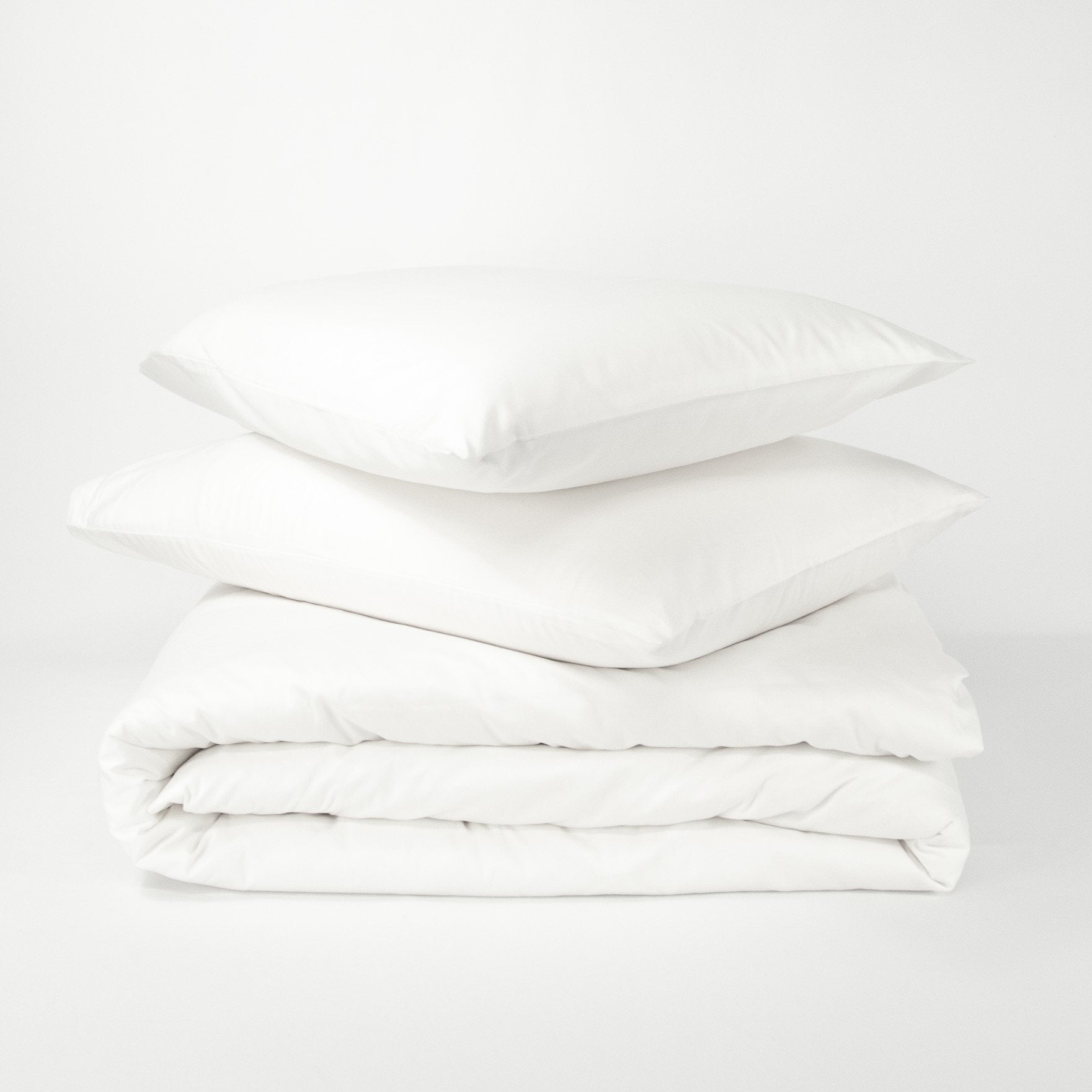 Stack of organic cotton quilt cover set with pillowcases and folded quilt cover in pure white