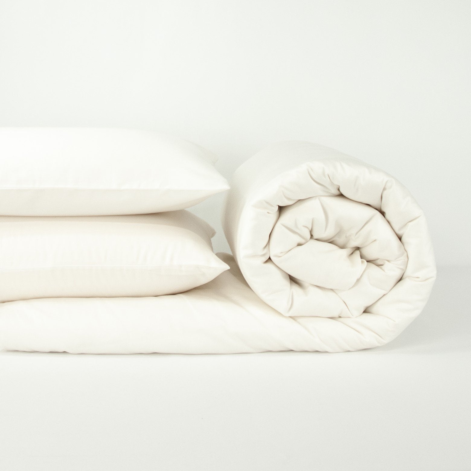 Stack of organic cotton quilt cover set with pillowcases and rolled up quilt cover in warm white