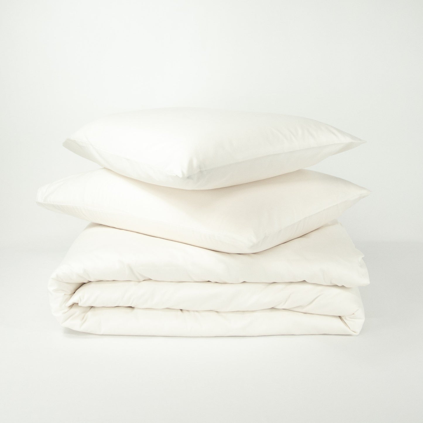 Stack of organic cotton quilt cover set with pillowcases and folded quilt cover in warm white