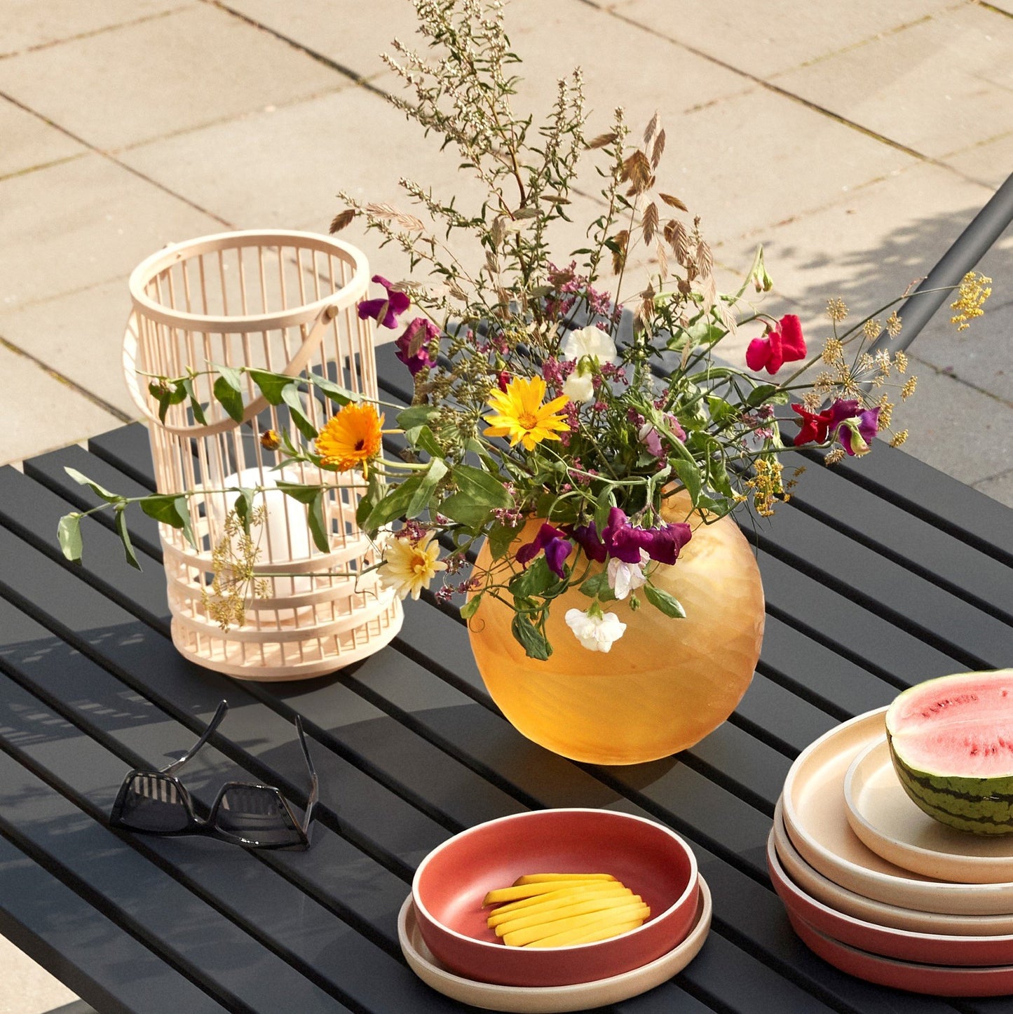 Hubsch Interior Scandi style round dune textured vase in amber gold glass on a black outdoor dining table with plates