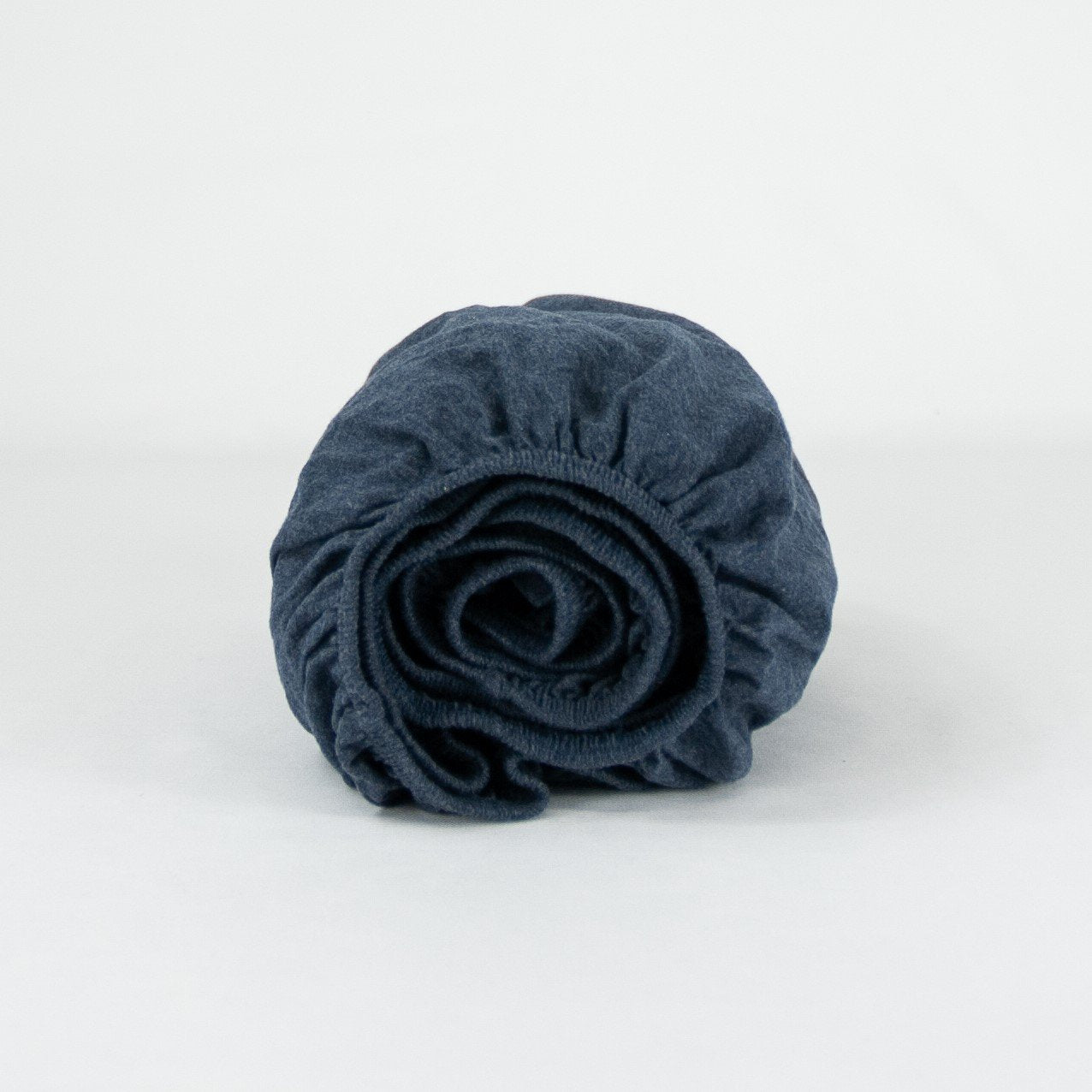 Rolled up organic cotton fitted cot sheet in indigo blue