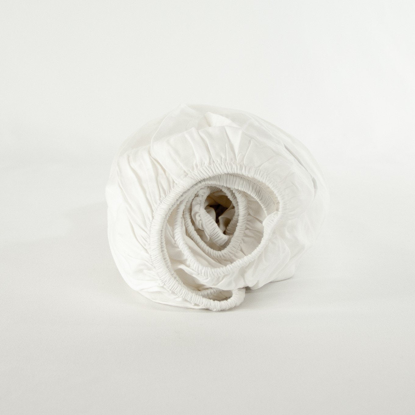 Rolled up organic cotton fitted cot sheet in pure white