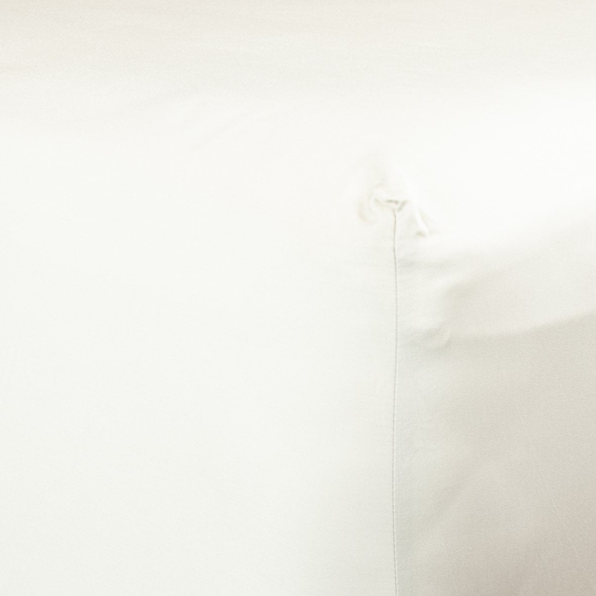Corner of bed with organic cotton fitted sheet in warm white