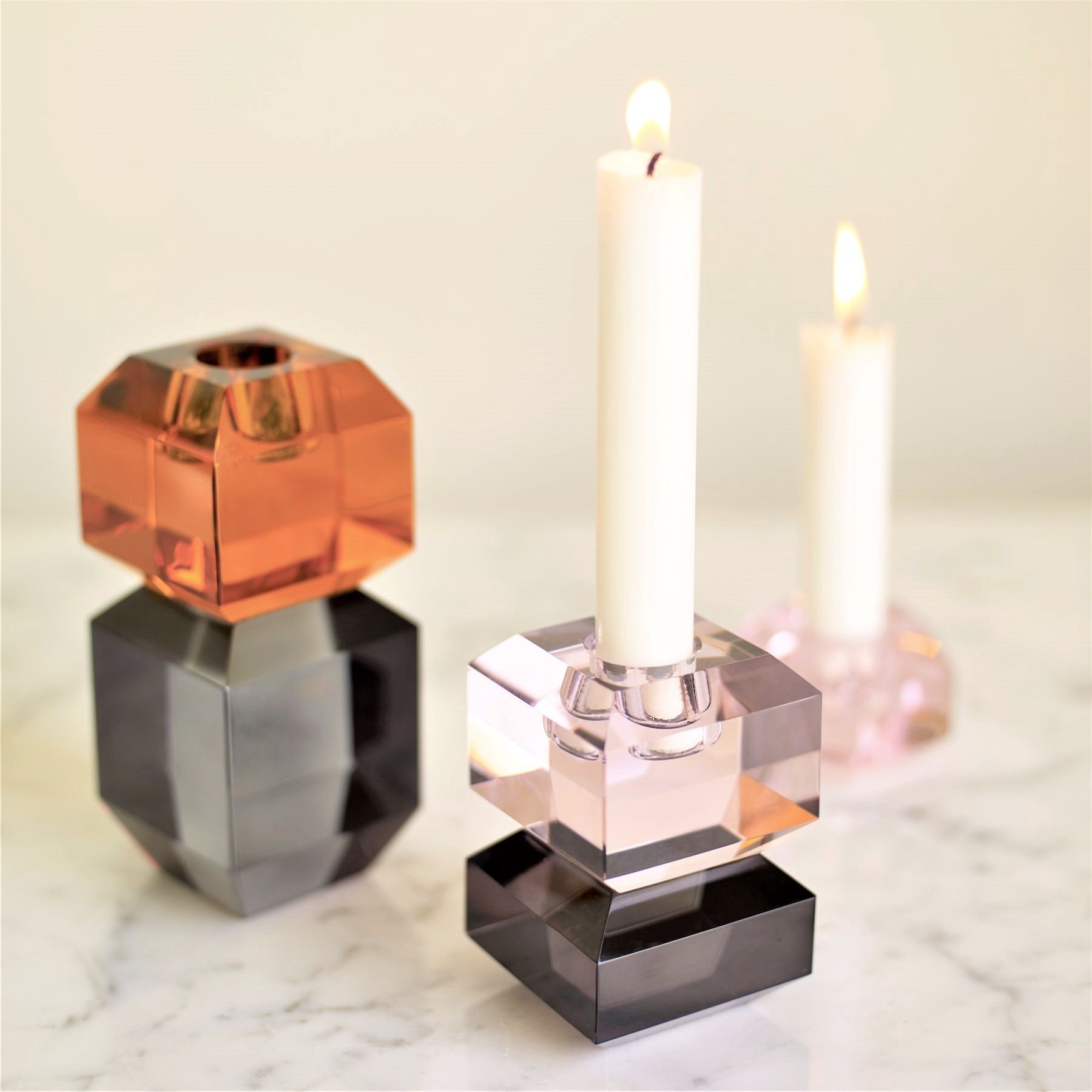 Hubsch Interior modern gem-like candle holders in amber, grey and pink glass on marble table with lit candles in them