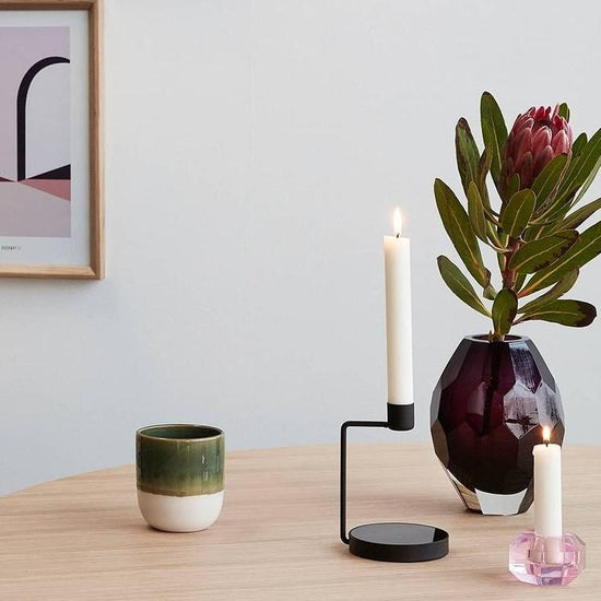 Hubsch Interior modern candle holder in pink glass, on a wood table with protea flower, candlestick and coffee cup