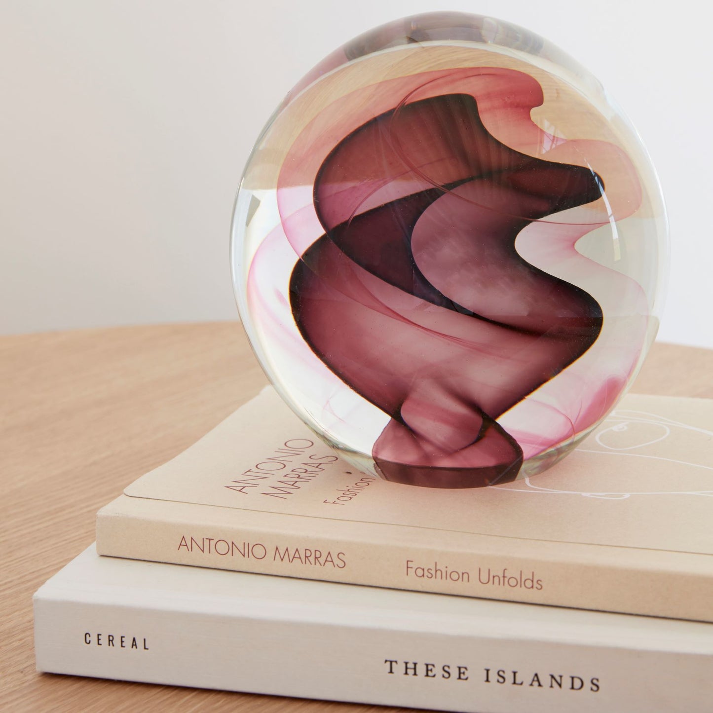 Close up of a Hubsch Interior objet d’art paperweight in burgundy red and pink swirl pattern on coffee table with books