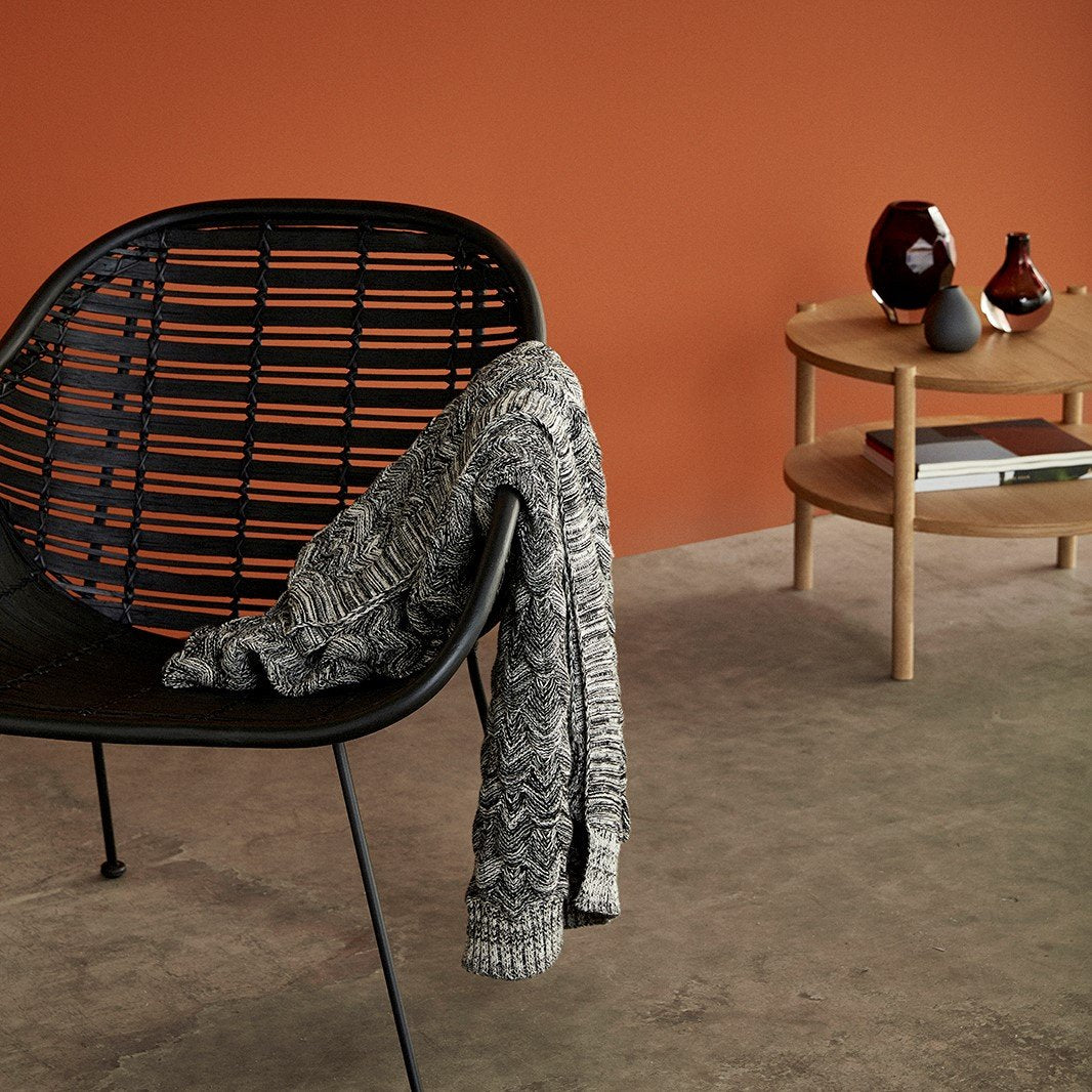 Hubsch Interior Scandi designer scale knit throw blanket on black rattan chair with round wood table in the background