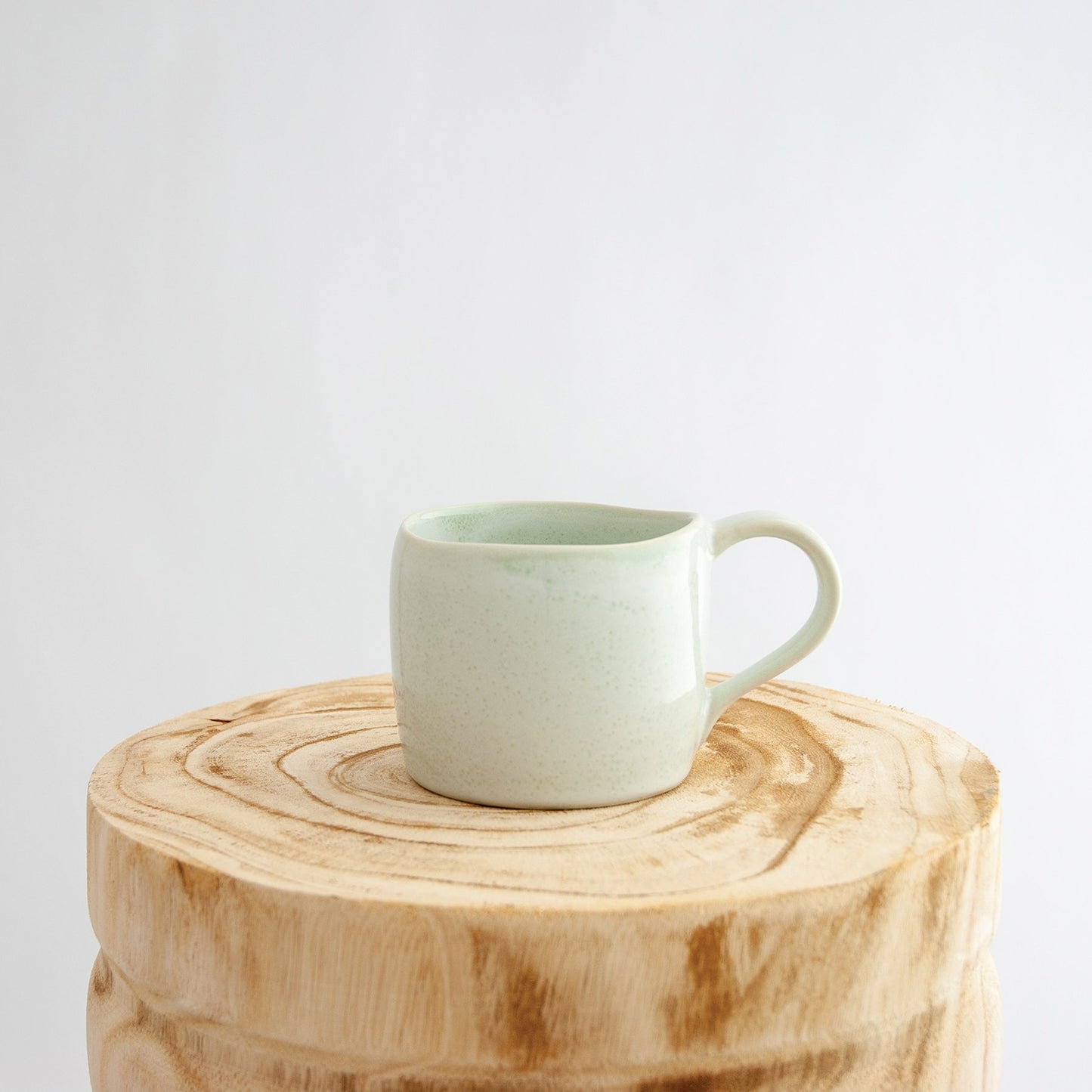 Robert Gordon moss green organic mug coffee cup sitting on a natural wooden round side table
