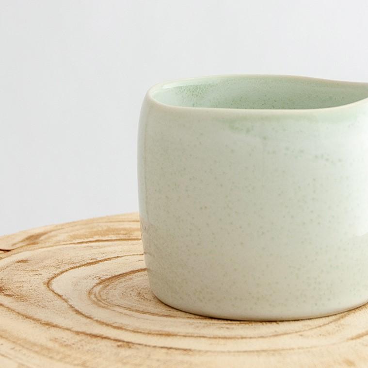Close up of a Robert Gordon moss green organic mug coffee cup sitting on a natural wooden round side table