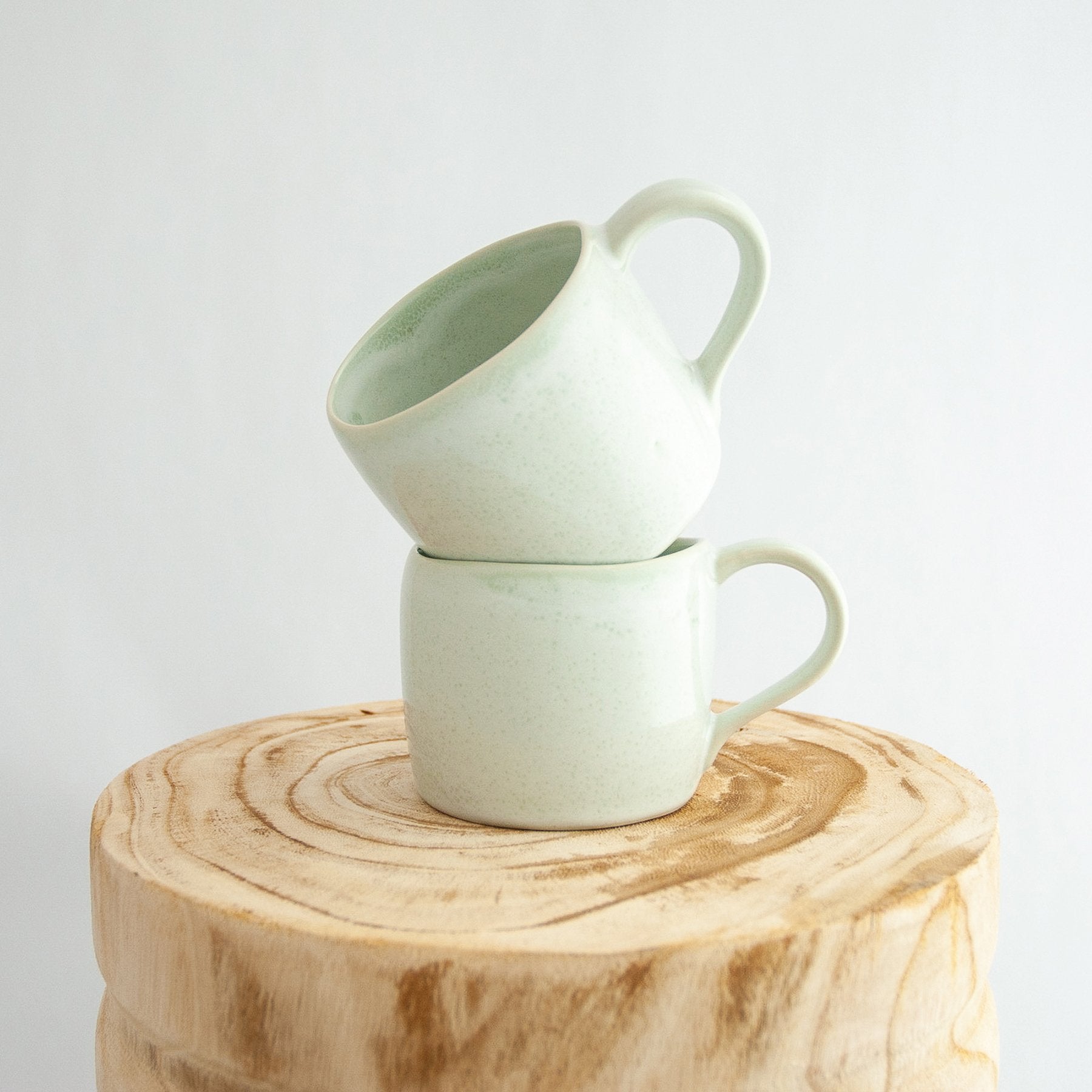 Two Robert Gordon moss green organic mugs stacked on a natural wooden round side table