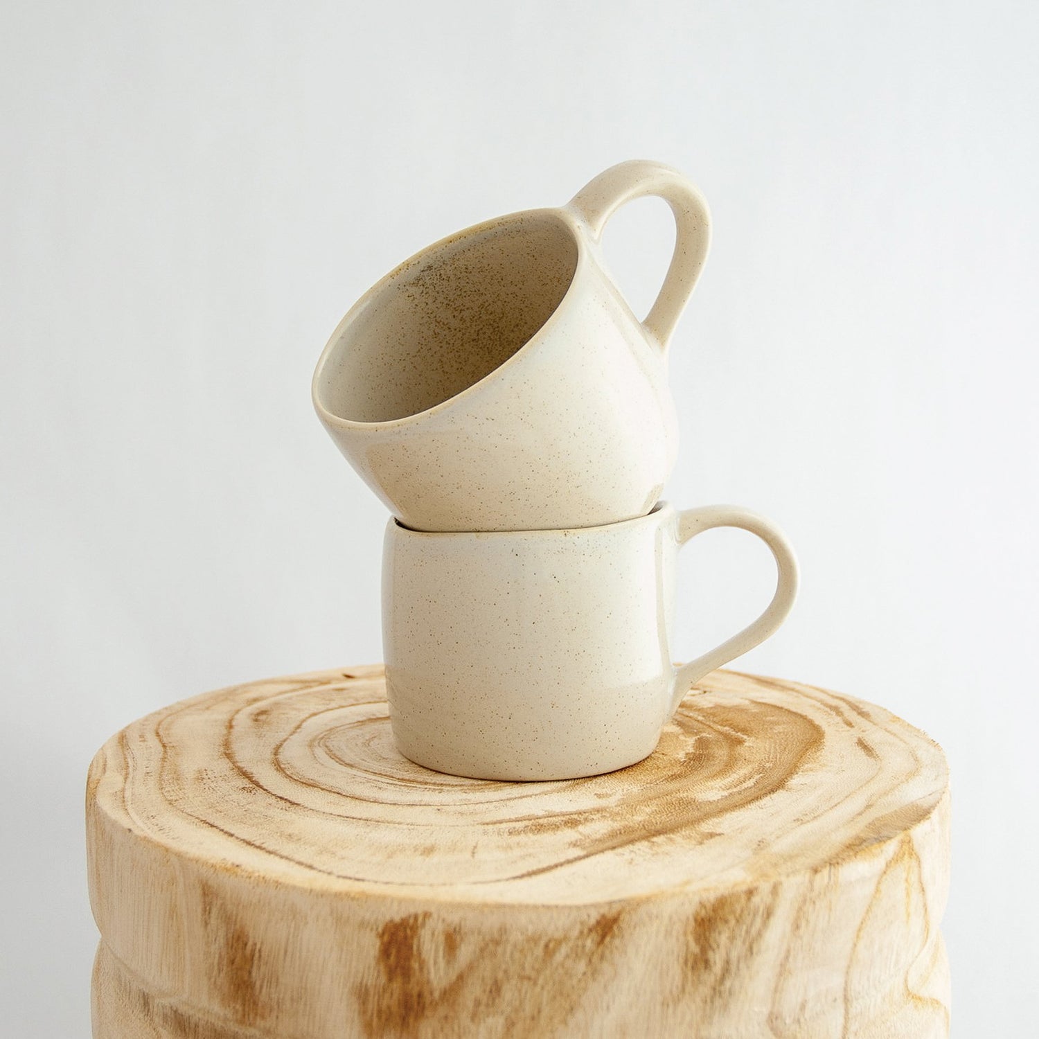 Two Robert Gordon oatmeal cream organic mugs stacked on a natural wooden round side table