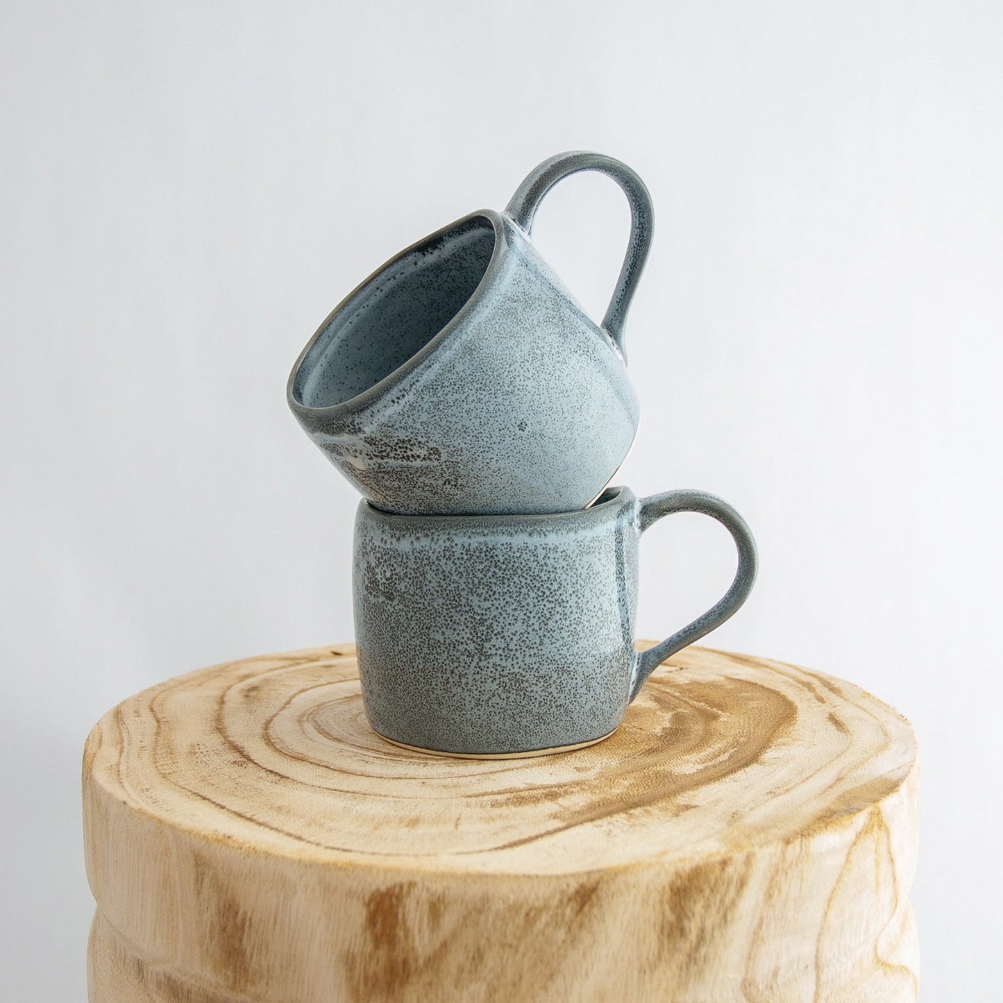 Two Robert Gordon storm grey organic mugs stacked on a natural wooden round side table