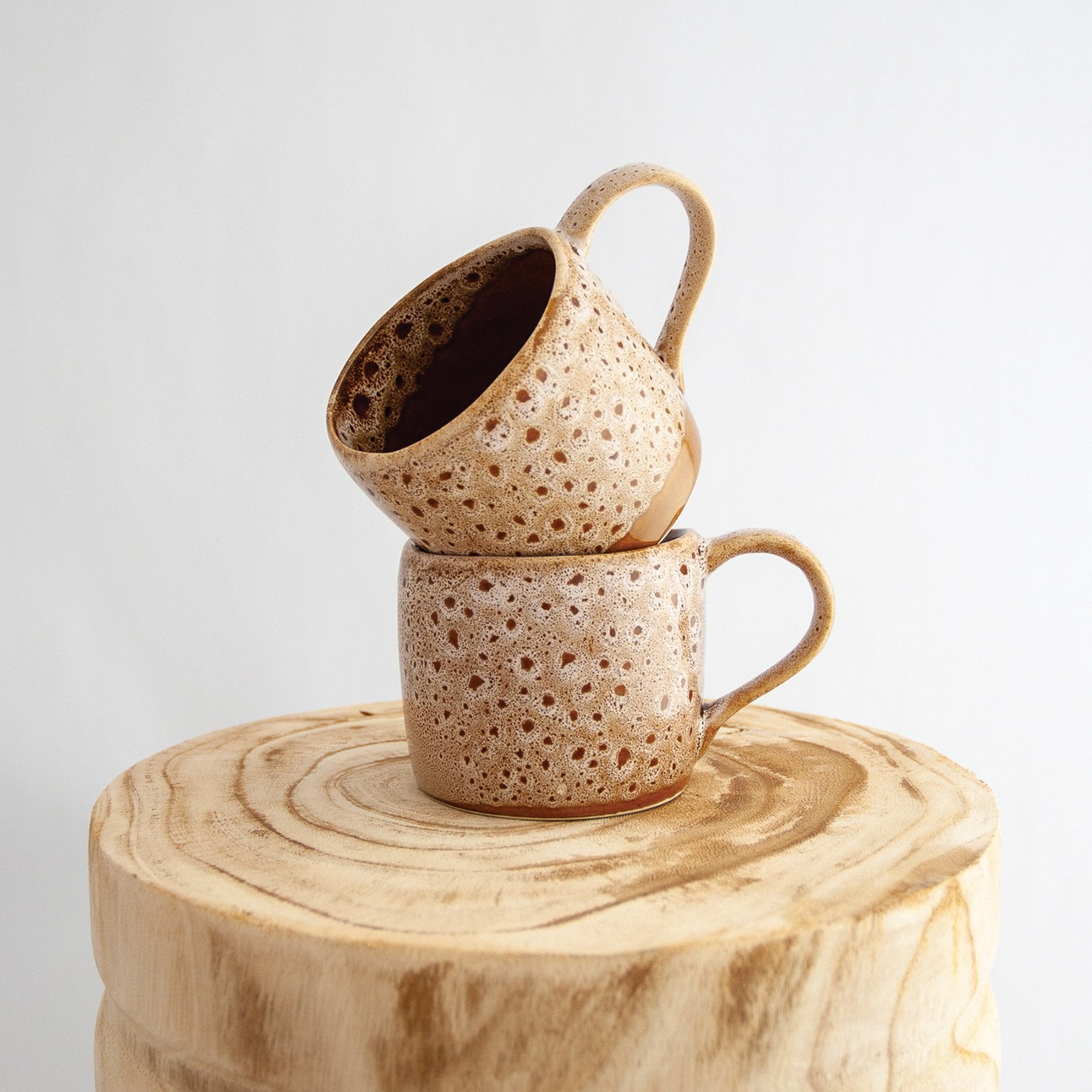 Two Robert Gordon white ochre organic mugs stacked on a natural wooden round side table