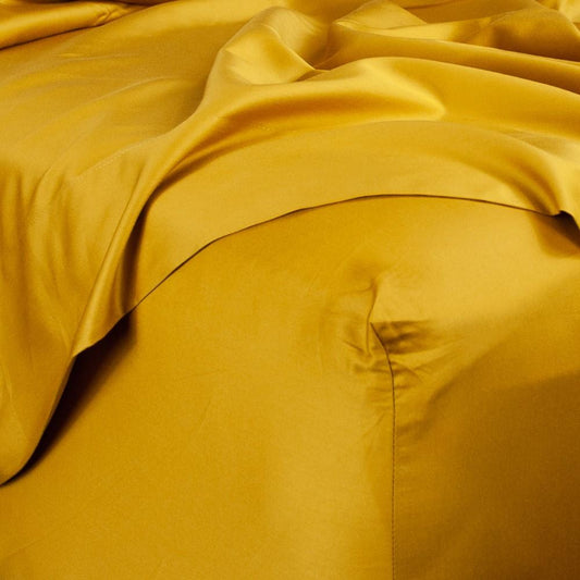 Corner of bed with organic cotton fitted sheet and top sheet in honey gold