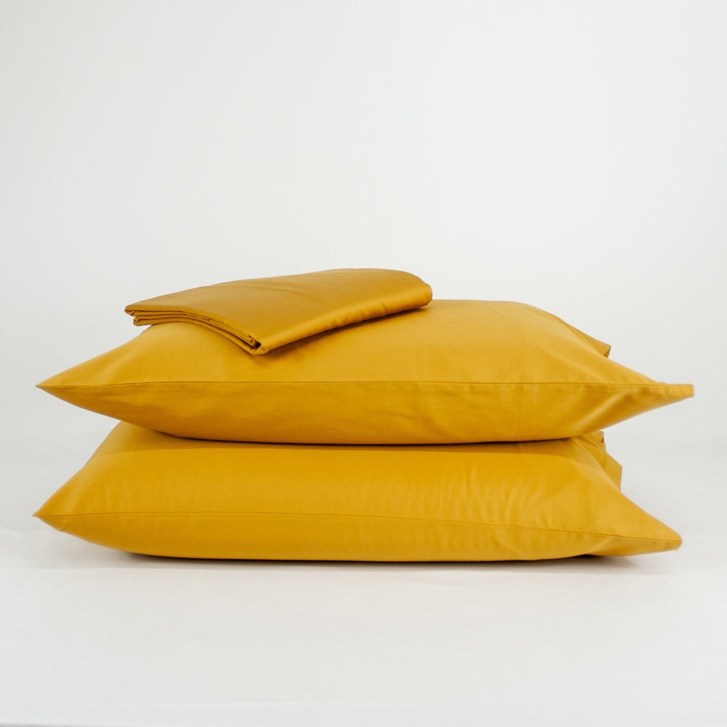 Stacked organic cotton pillowcases and sheets in honey gold