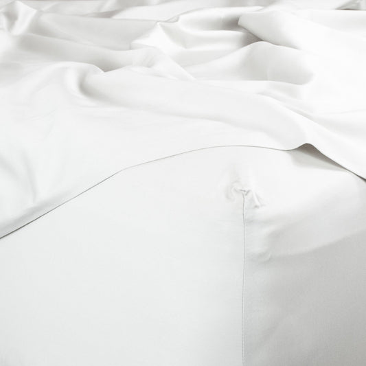 Corner of bed with organic cotton fitted sheet and top sheet in pure white