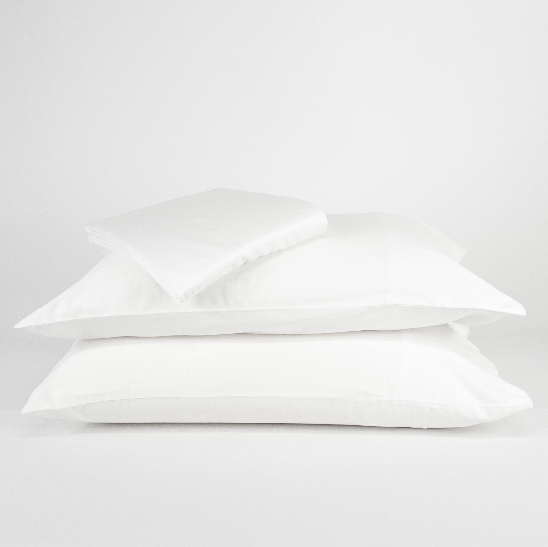 Stacked organic cotton pillowcases and sheets in pure white