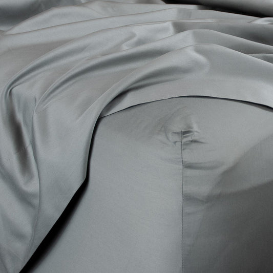Corner of bed with organic cotton fitted sheet and top sheet in sleet grey