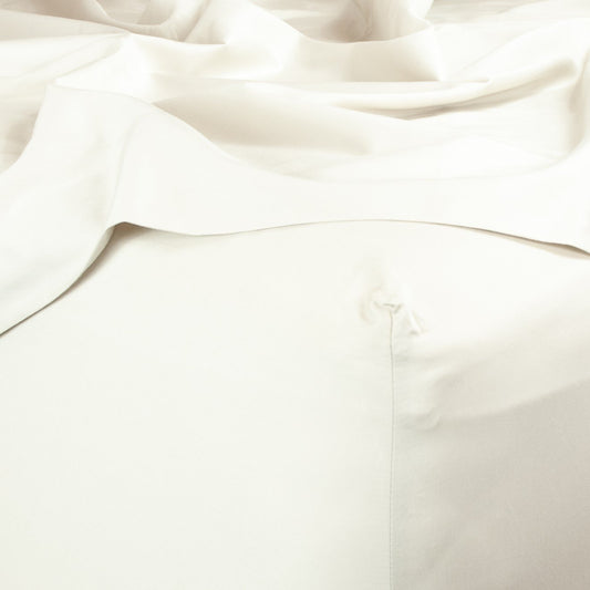 Corner of bed with organic cotton fitted sheet and top sheet in warm white
