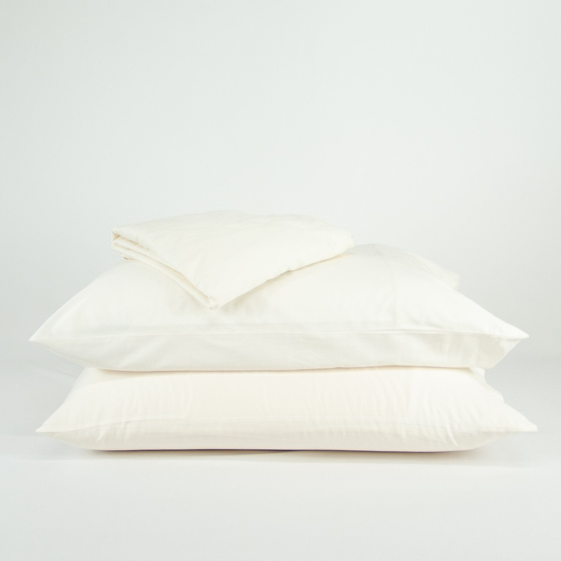 Stacked organic cotton pillowcases and sheets in warm white