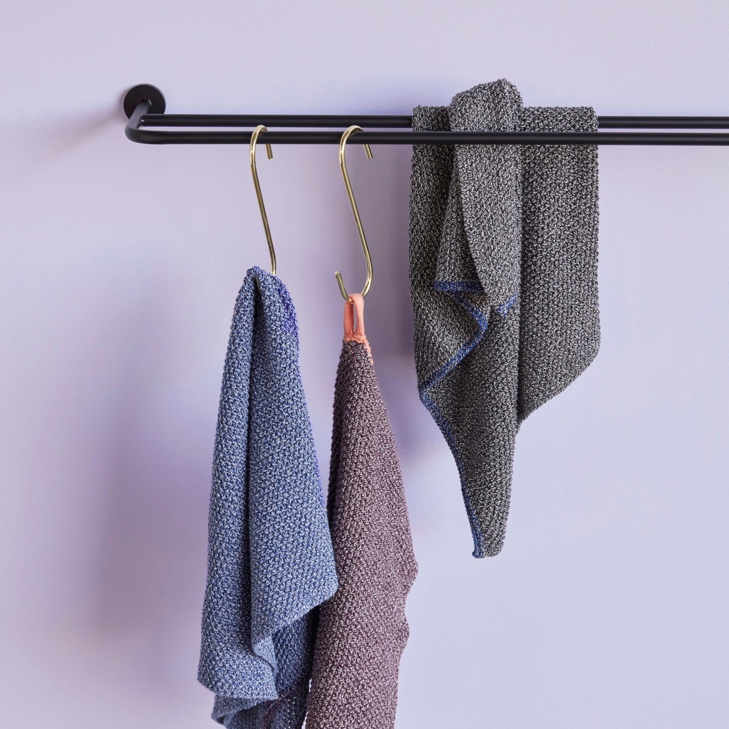Three Hubsch Interior Scandi designer tea towels in various colours of cotton knit, hanging from a black towel rail