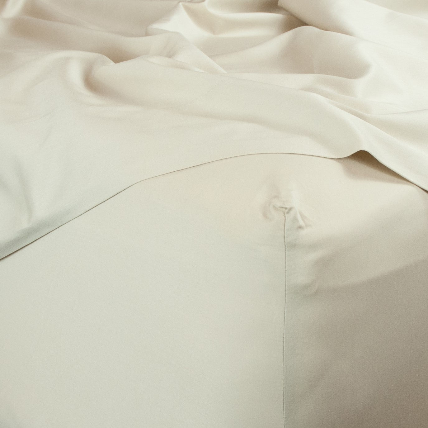 Corner of bed with organic cotton fitted sheet and top sheet in egg shell white